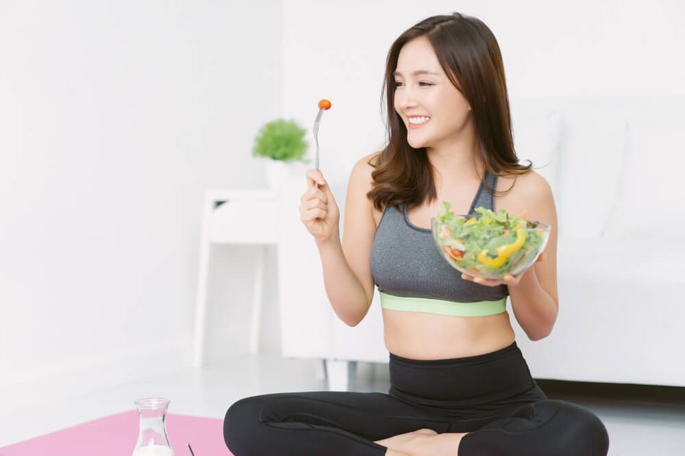 tóc sâu cố gái mặc đồ thể thao đang ngồi xếp bằng và cầm bát đựng salad