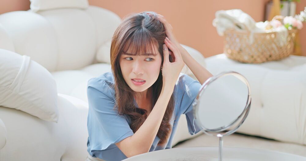 tóc sâu cô gái đang rẽ tóc và quan sát tóc qua gương với vẻ mặt lo lắng