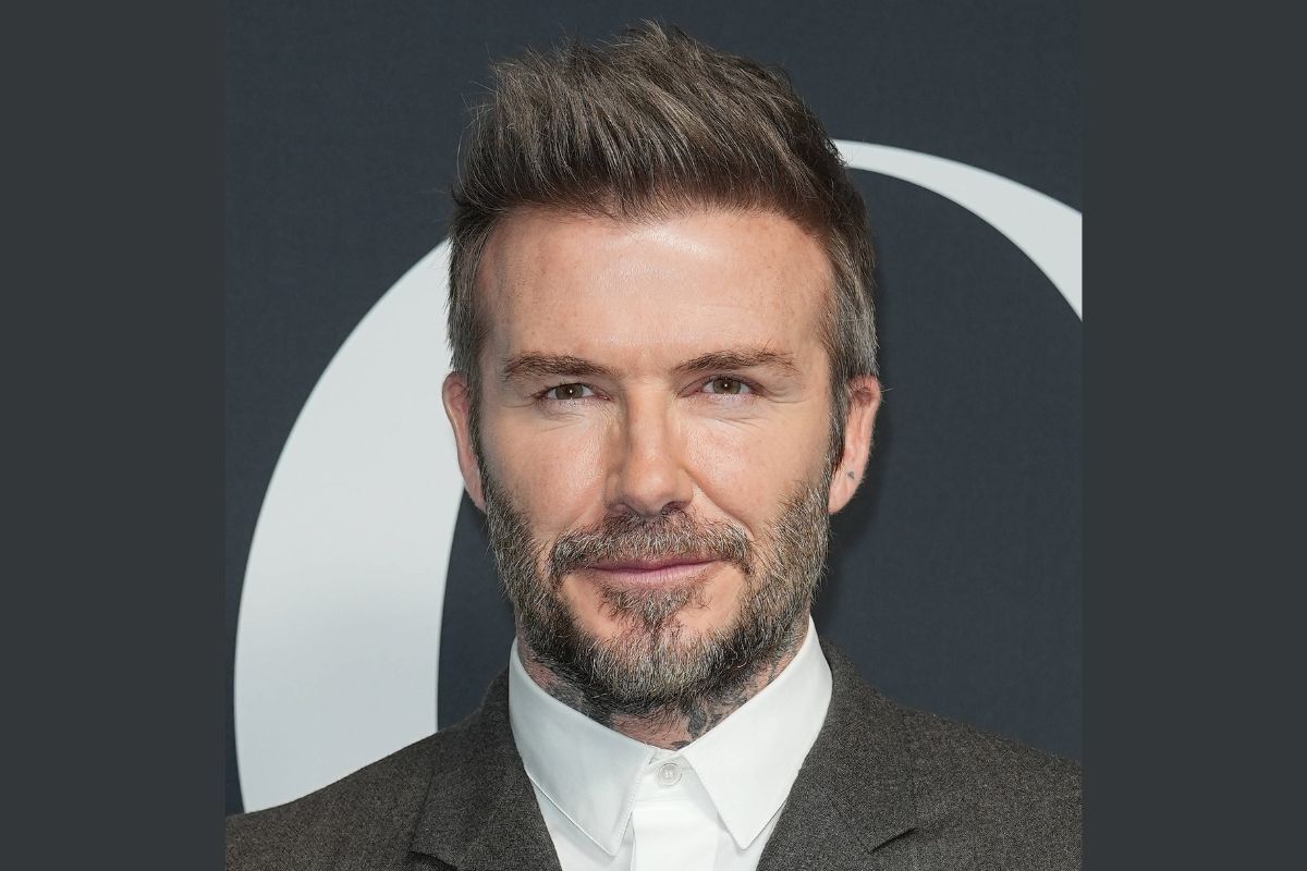 Kiểu tóc của David Beckham mặc vest màu ghi và sơ mi màu trắng trên phông nền đen