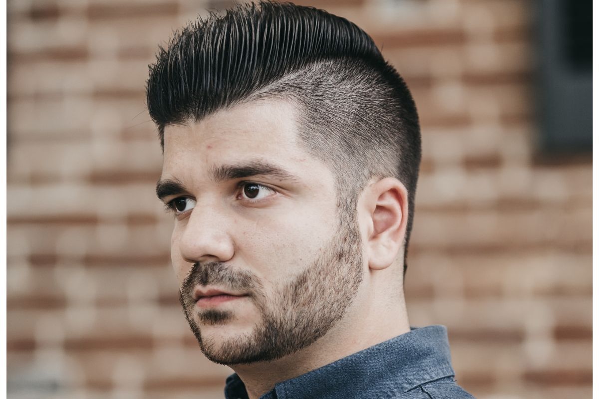 tóc mohican người đàn ông mặc áo denim đứng trước bức tường gạch