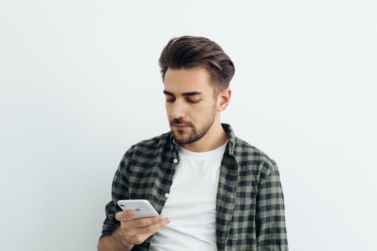 kiểu tóc sport đẹp người đàn ông đang xài điện thoại trên nền tường trắng