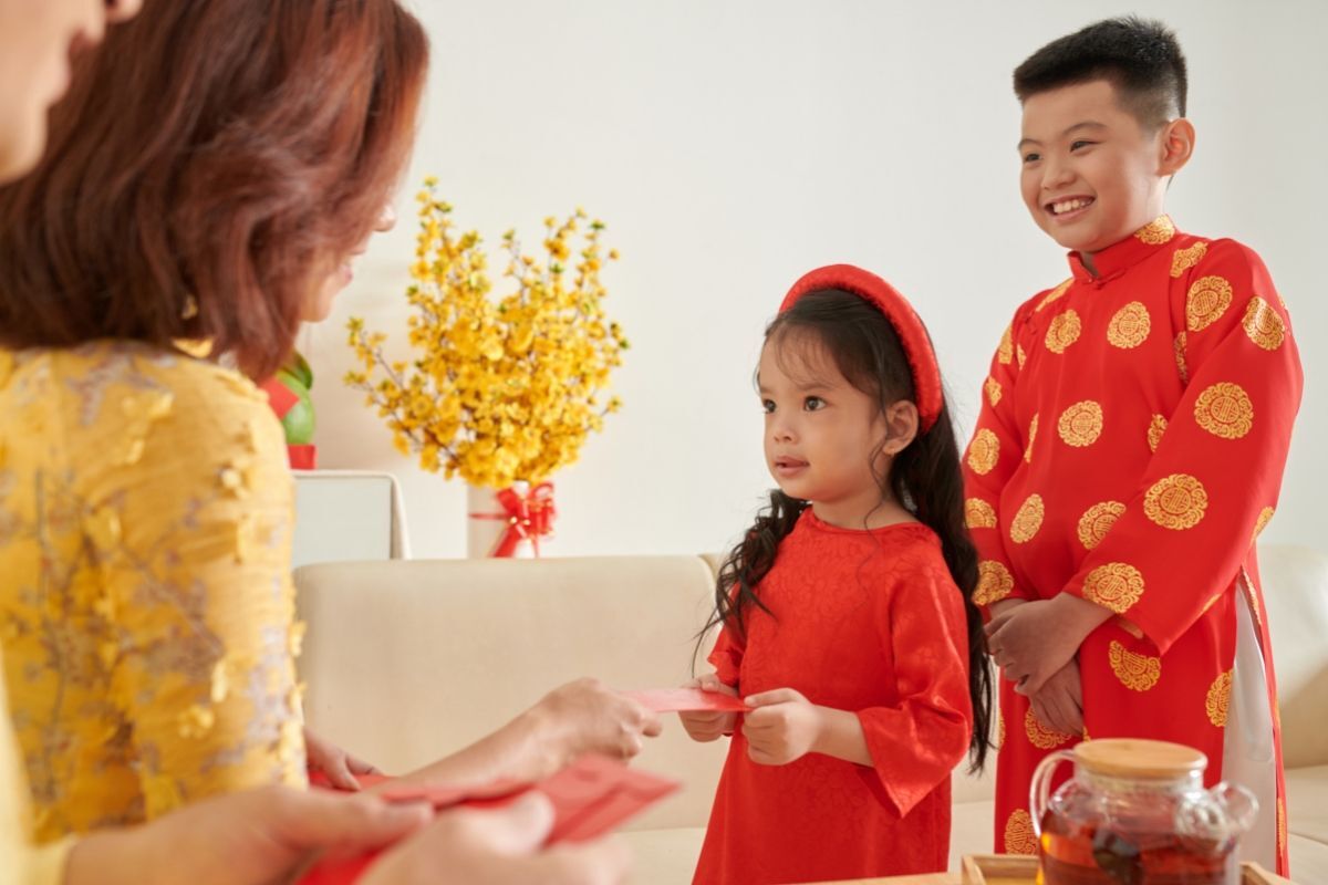 Còn bao nhiêu ngày nữa đến Tết 2023 hai trẻ em mặc áo dài đỏ xếp hàng nhận lì xì