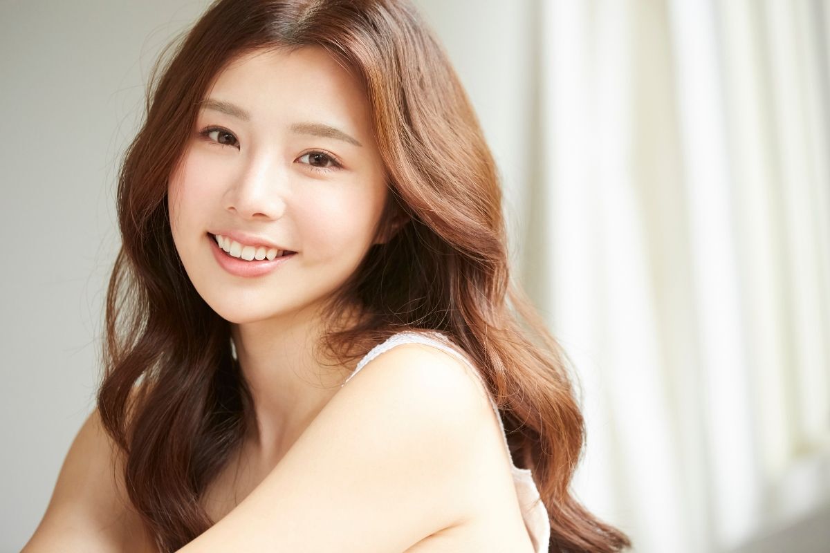 Tóc layer xoăn sóng nước cô gái ngồi trong phòng phía sau là rèm cửa màu trắng