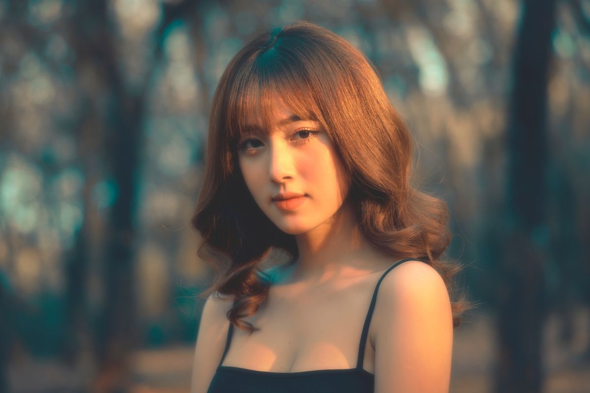 Tóc dài xoăn sóng cô gái mặc váy dây màu đen đang đứng dưới ánh nắng chiều