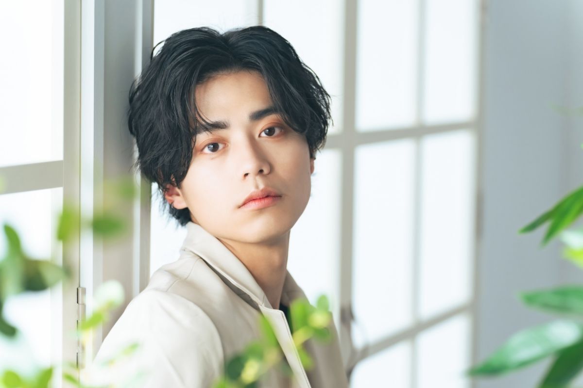 tóc nam 2023 đẹp chàng trai tóc rẽ ngôi giữa xoăn nhẹ tựa lưng vào cửa sổ 