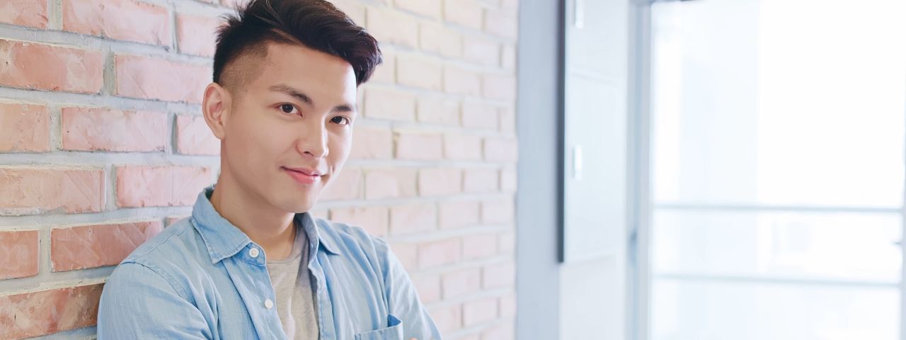 tóc layer nam ngắn chàng trai mặc áo sơ mi màu xanh khoanh tay dựa lưng vào tường