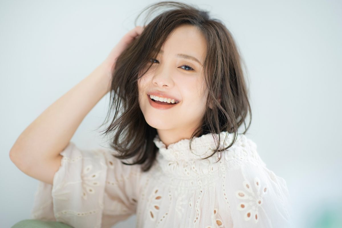 Tóc duỗi cụp layer cô gái mặc áo trắng có hoạ tiết thêu hoa đang cười rạng rỡ