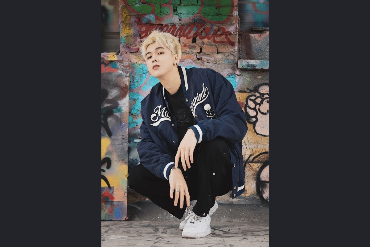 Thời trang đường phố Hàn Quốc chàng trai nhuộm tóc bạch kim ngồi trước bức tường có nhiều hình vẽ