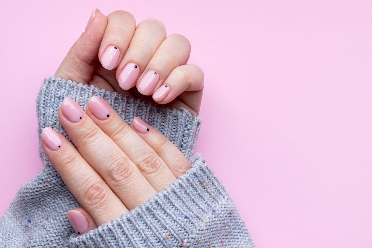 Nail màu hồng thạch bàn tay mặc áo len xám trên nền hồng