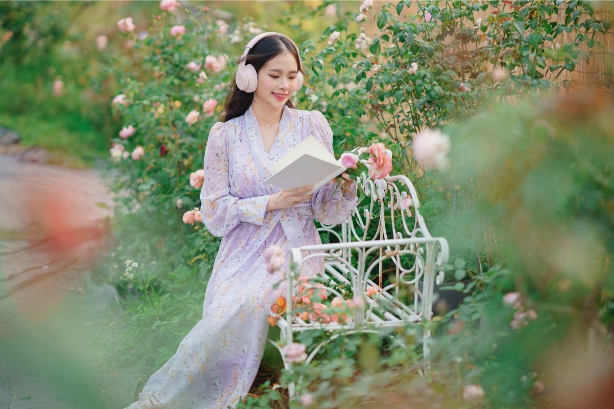 cottagecore là gì cô gái mặc đầm hoa màu tím đeo headphone đọc sách ngoài vườn