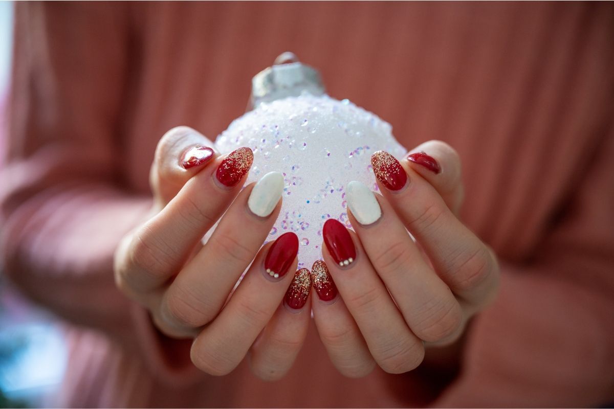 nail noel bàn tay cầm trái châu màu trắng ngón tay màu đỏ phủ kim tuyến vàng xen kẽ móng trắng và móng đỏ đính đá trắng