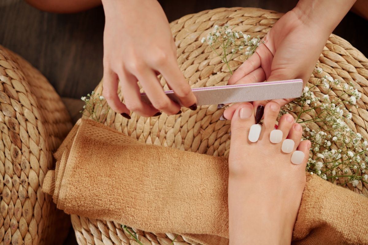 Nail chân đính đá sang trọng bàn chân đang được chăm sóc với dũa móng và đệm cói