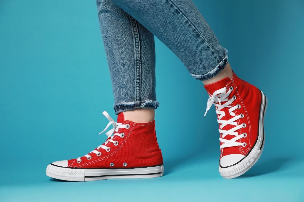các hãng giày nổi tiếng đôi chân phụ nữ mặc quần jean dài mang giày converse màu đỏ trên nền xanh ngọc