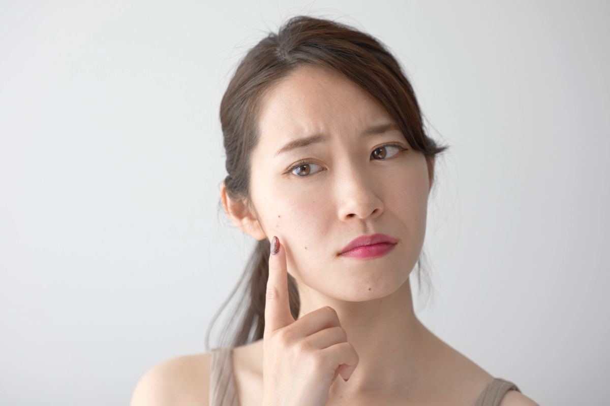 cách trị mụn ẩn cô gái cau mày, chỉ ngón tay trỏ lên má