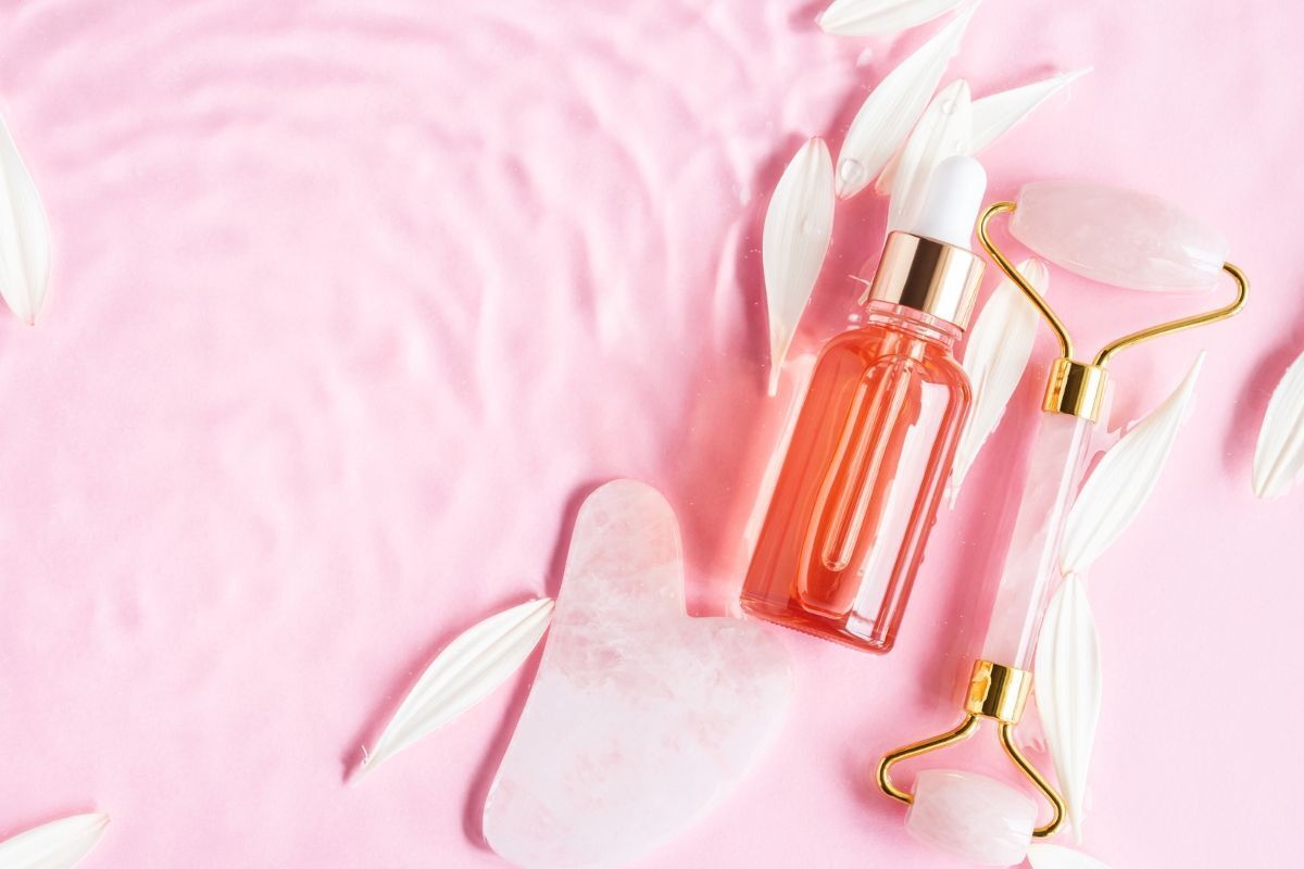 các bước skincare ban đêm chai dầu dưỡng da mặt màu hồng nằm kế gua sha và thanh lăn