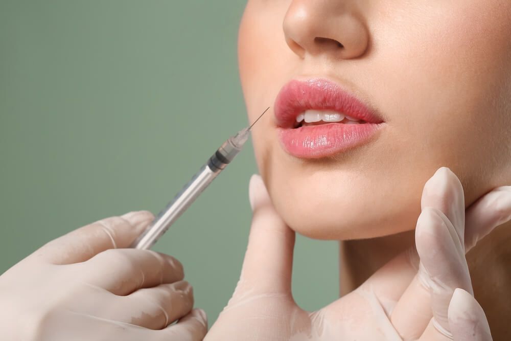 cách trị thâm môi tiêm filler cho môi bàn tay đeo găng tay màu trắng đang cầm mũi tiêm hướng về phía đôi môi hồng