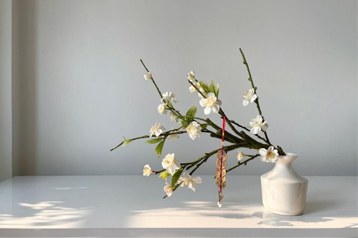 Cành hoa tuyết mai cắm trong lọ sứ màu trắng có treo dây đồng xu