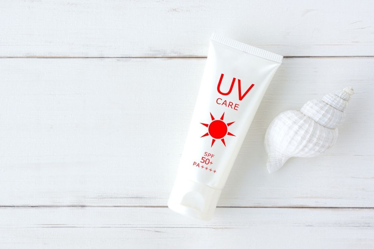 Bôi kem chống nắng đúng cách tuýp kem chống nắng màu trắng chữ màu đỏ đặt cạnh một chiếc vỏ ốc màu trắng