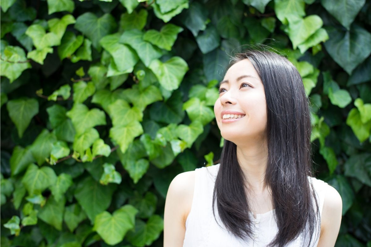 kiểu tóc cho người tóc mỏng đẹp cô gái tóc đen nhìn nghiêng mỉm cười sau lưng là nền lá màu xanh