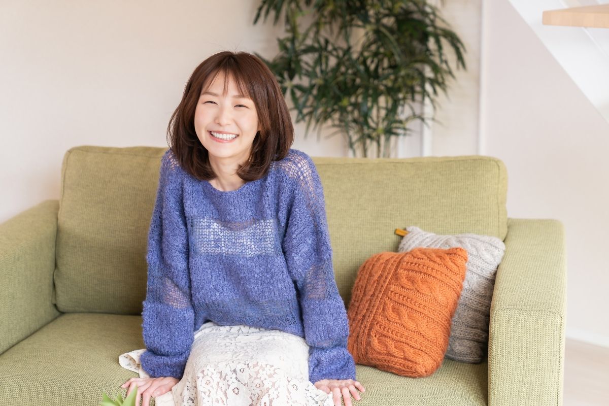 màu nhuộm tóc ngắn uốn cô gái mặc áo len màu xanh đen cười tươi ngồi trên ghế sofa tóc ngang vai cụp màu đỏ đồng