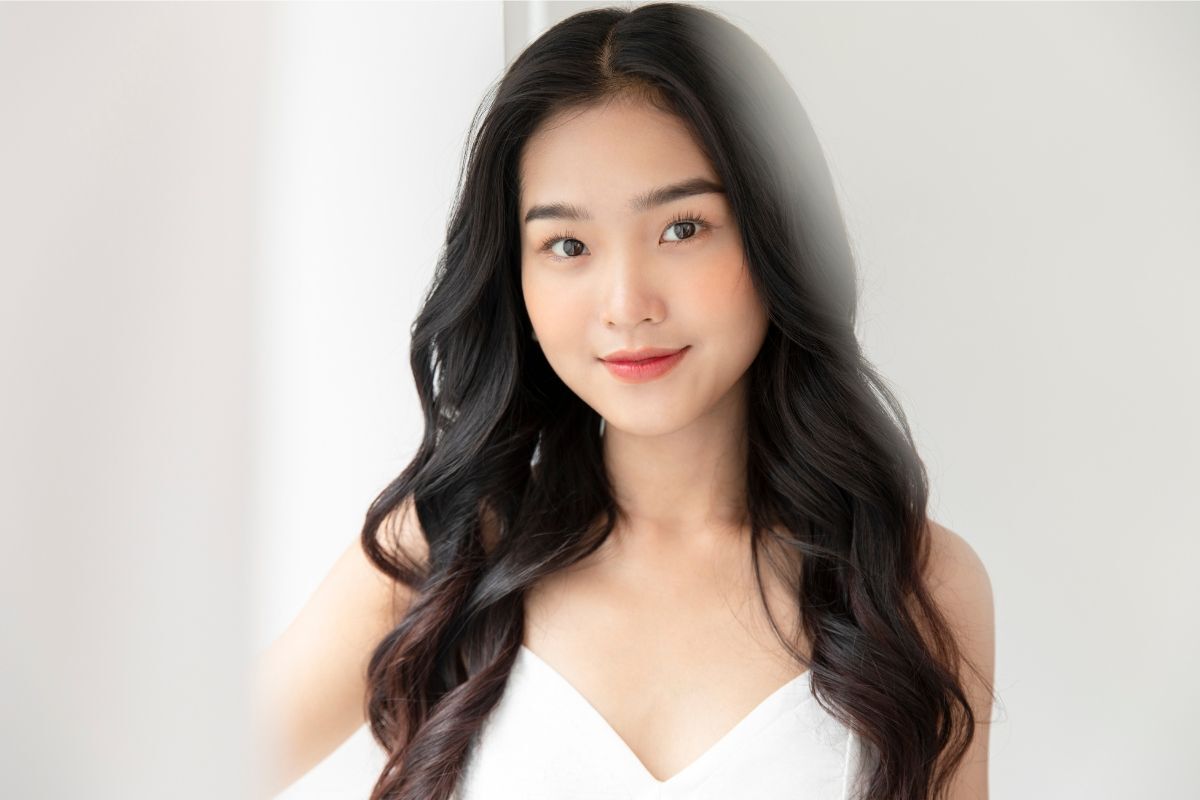 Cô gái mặc váy trắng cổ chữ V có mái tóc mái rẽ ngôi giữa và uốn xoăn