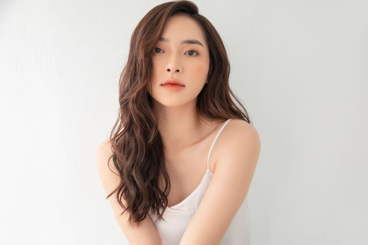 Cô gái có mái tóc xoăn nhẹ rẽ ngôi tóc mái lệch chụp trên nền tường trắng