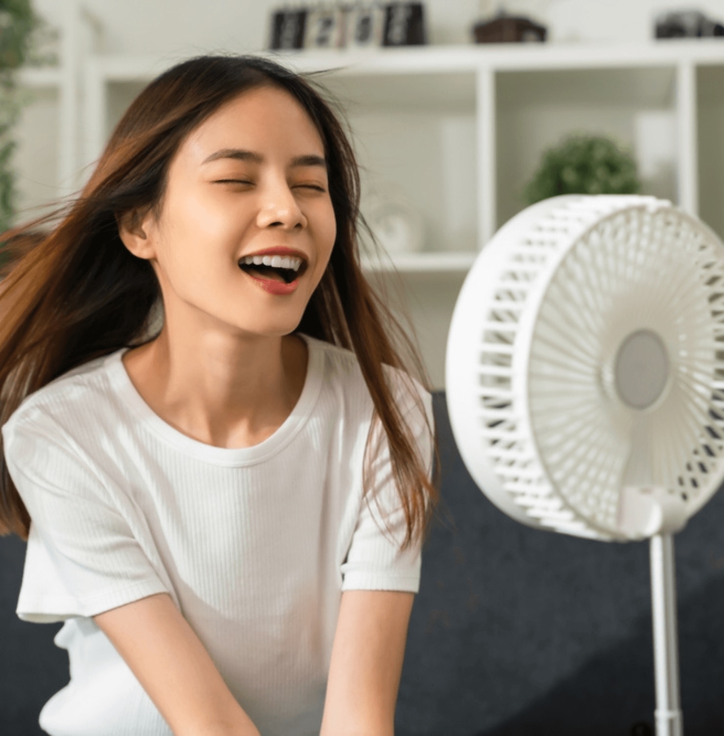 nên sấy tóc hay để khô tự nhiên nên sấy tóc bằng quạt hay máy sấy cô gái ngắm mắt ngồi trước quạt điện màu trắng.