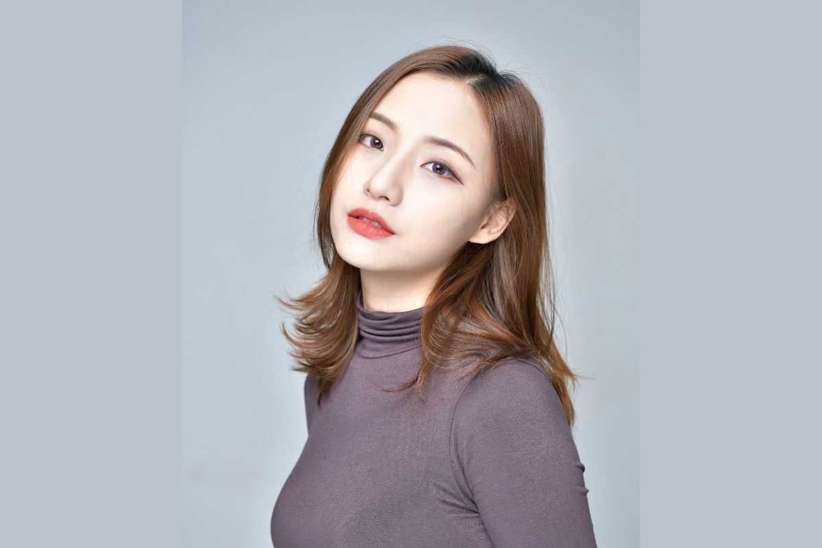 Tóc layer uốn nhẹ đẹp cô gái mặc áo cổ lọ màu tím chụp trên phông nền xám