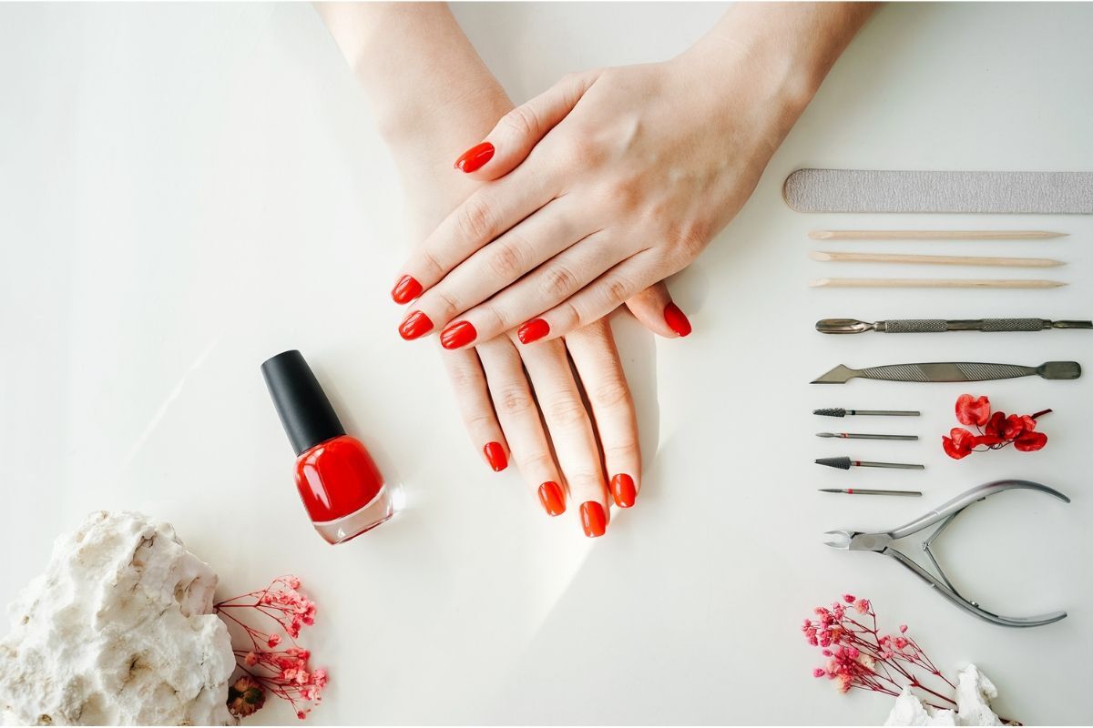 nail màu đỏ hai bàn tay sơn móng đỏ kế bên chai sơn màu đỏ kế bên bộ dụng cụ làm móng
