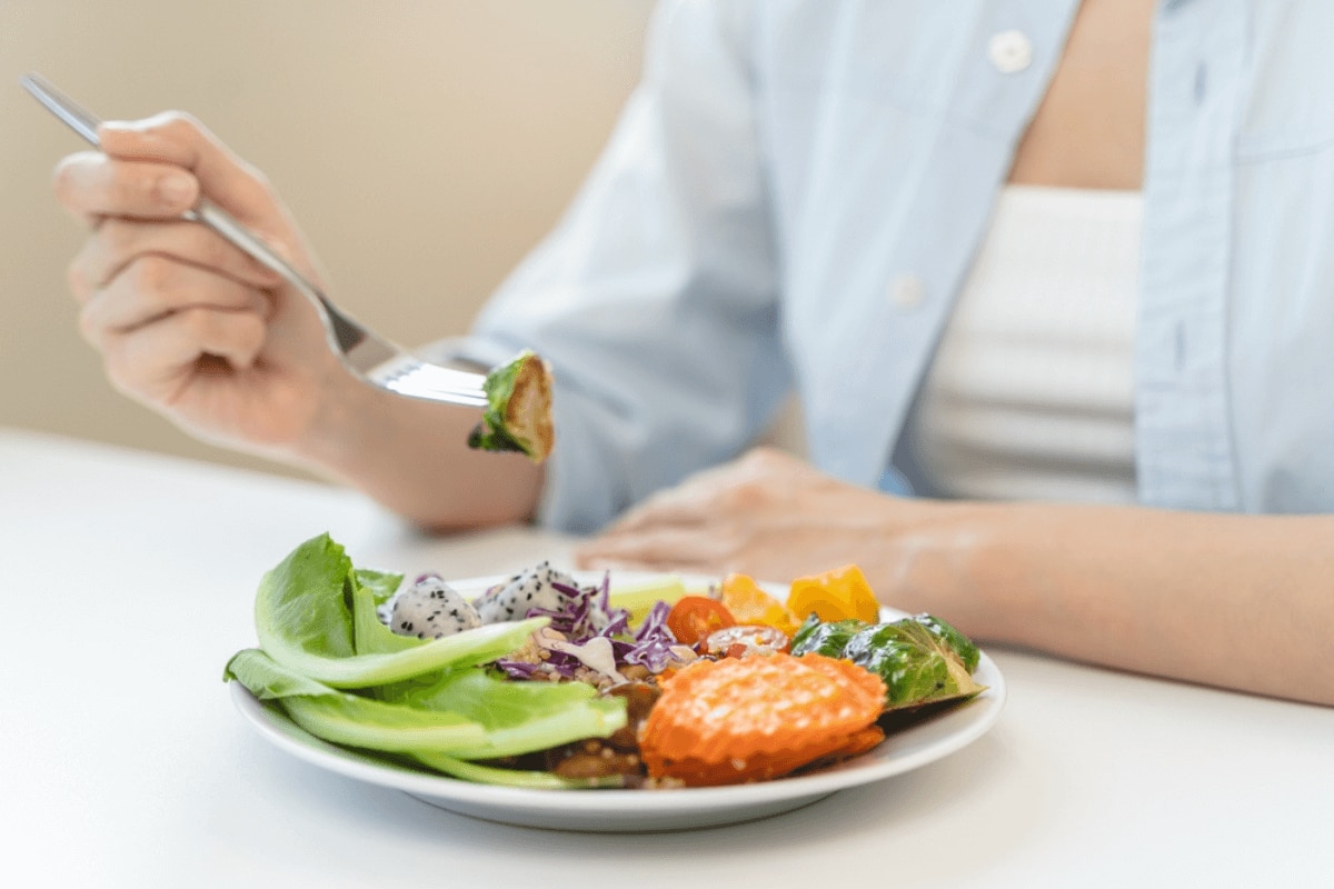 nguyên nhân rụng tóc ở nữ thiếu hụt chất dinh dưỡng cô gái chụp nửa người ngồi trên bàn cầm nĩa và dĩa đồ ăn