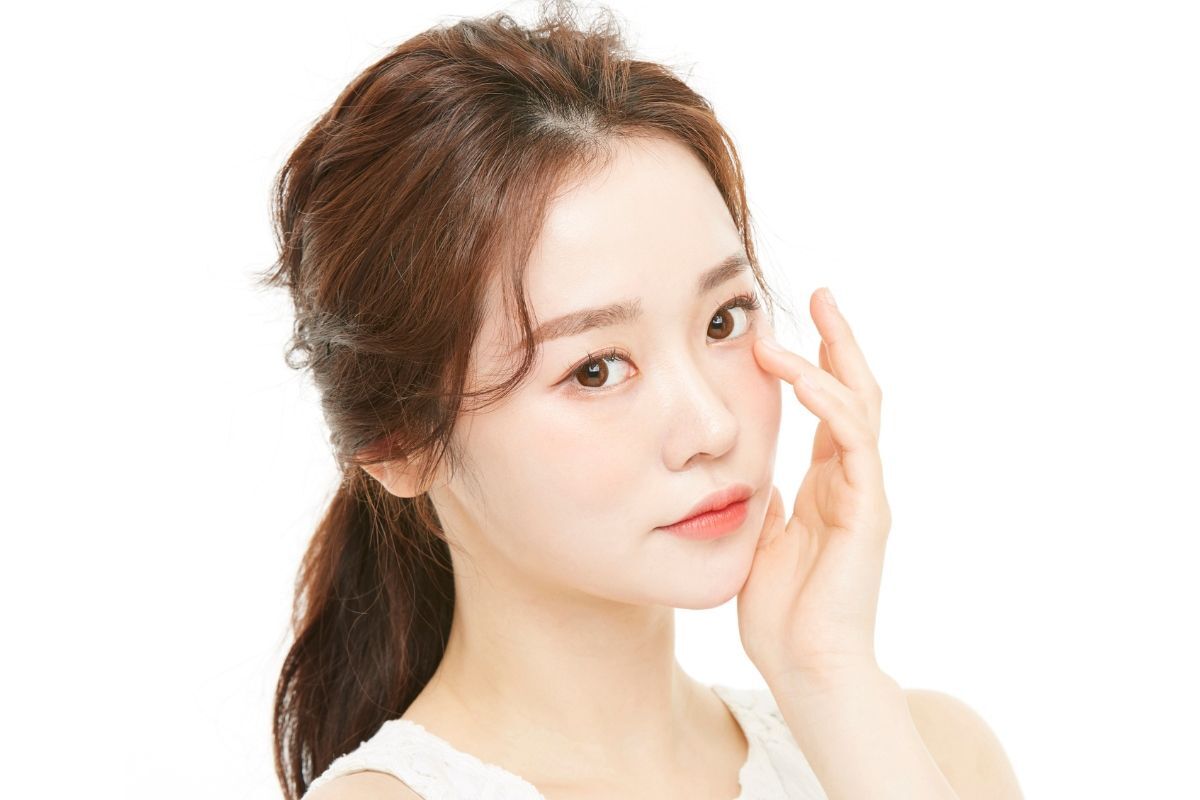 Phun xăm mí mắt cô gái buộc tóc đuôi ngựa thấp đang chạm một tay vào mặt