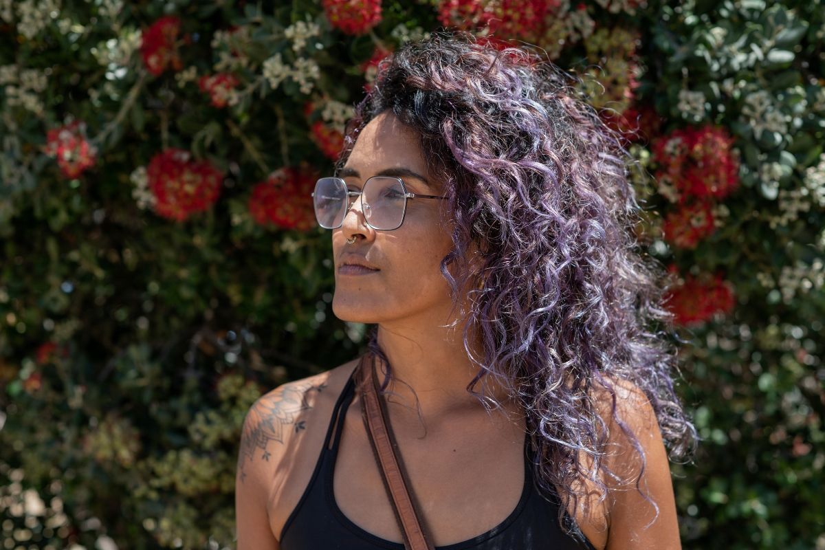 Nhan sắc lên hương với tóc nâu tây ánh rêu màu tóc quyến rũ và chuẩn hot trend 2022 cô gái tóc xoăn mặc áo ba lỗ đen phía sau là bụi hoa hồng đỏ