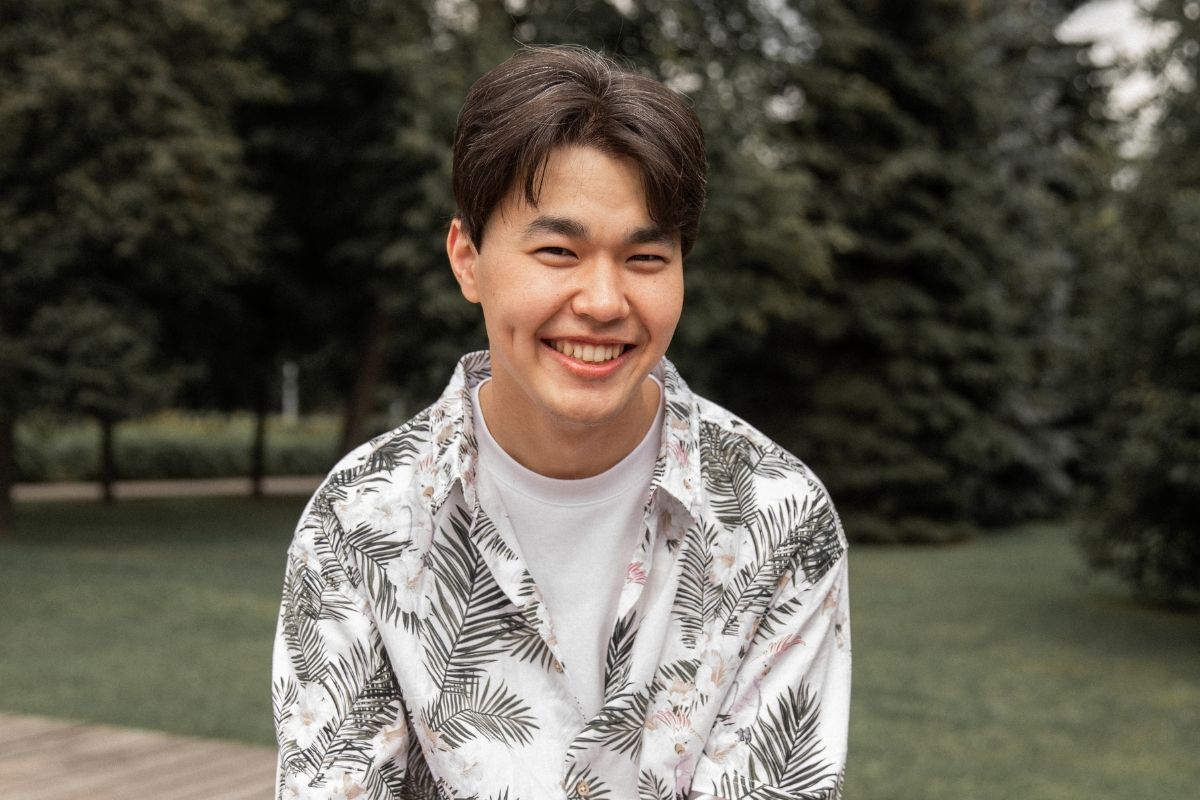 Tóc middle part chàng trai cười tươi mặc áo sơ mi hoạ tiết phía sau là vườn cây xanh