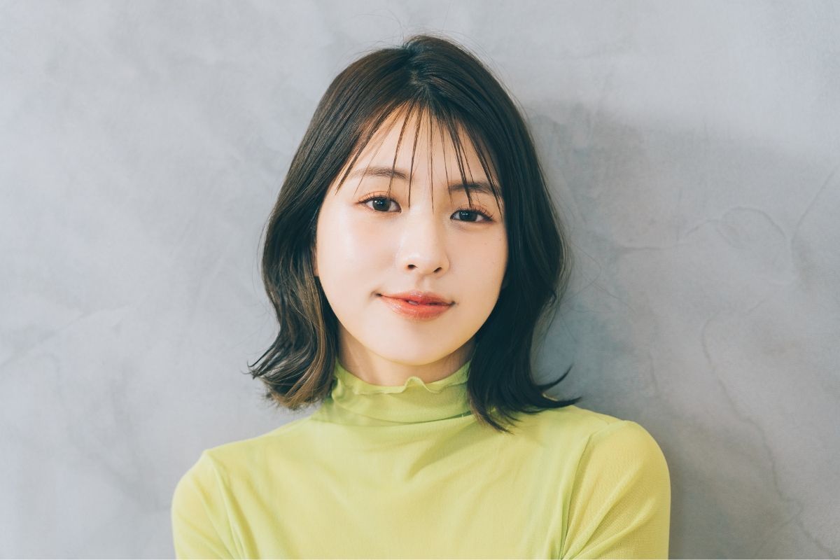 Tóc ngắn tỉa layer mái thưa cô gái mặc áo xanh cổ lọ mỉm cười dựa vào tường