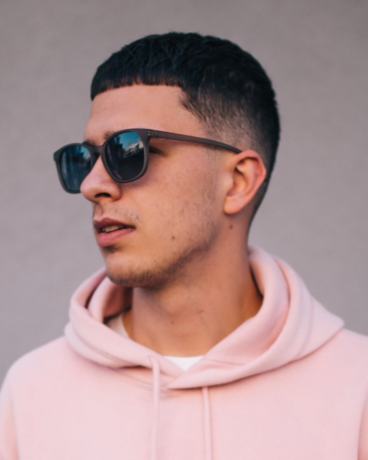 Tóc buzz cut tóc tóc buzz cut kết hợp textured crop fade chàng trai mặc áo màu hồng đang nhìn sang bên trái đeo kính đen 