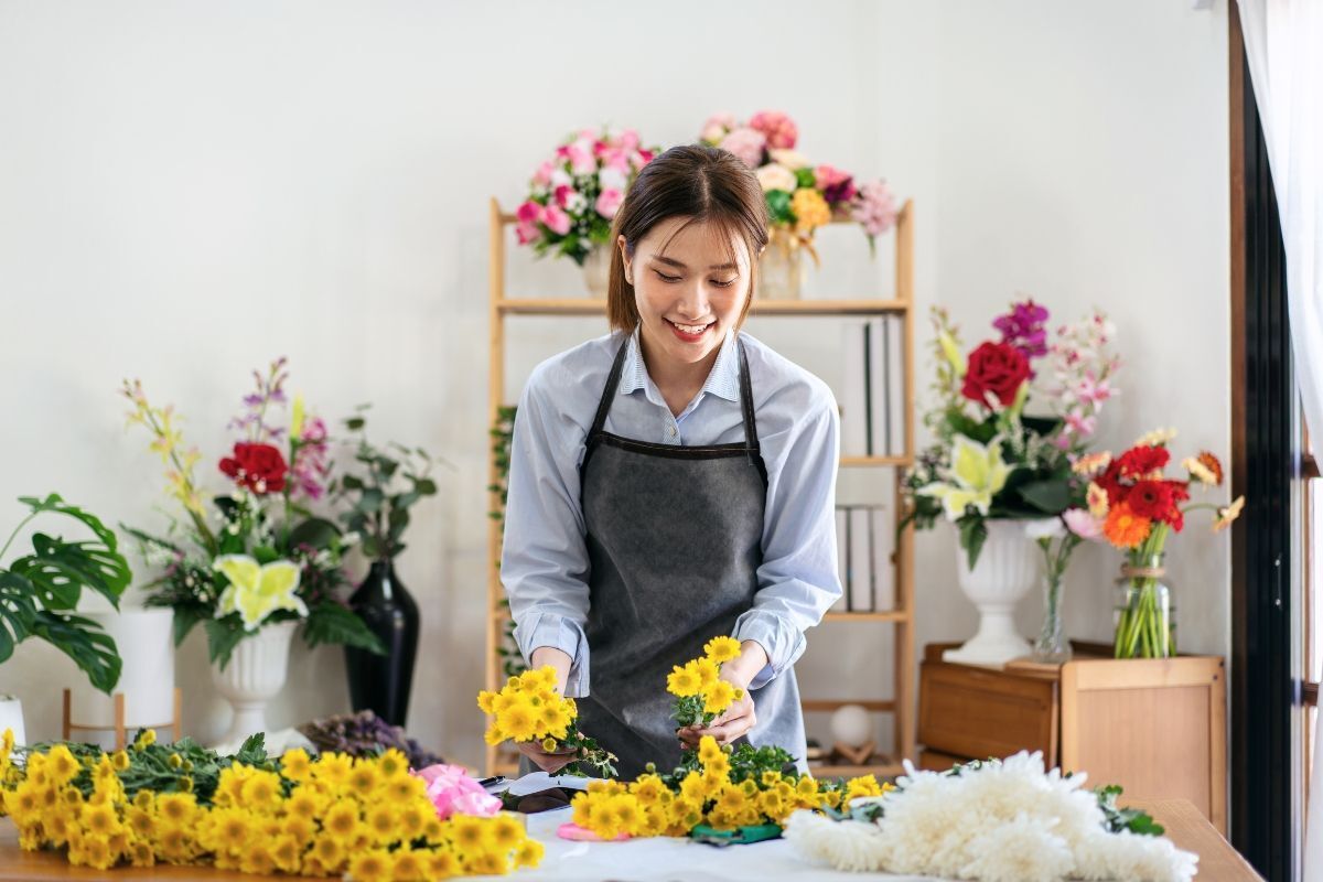 cách cắm hoa cúc cô gái đang cầm những nhành hoa cúc vàng trên bàn trong tiệm bán hoa