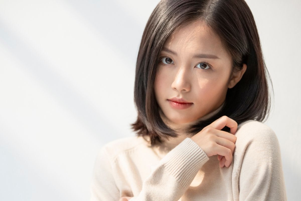 Tóc layer duỗi thẳng cô gái mặc áo len màu be đang chạm một tay lên vai