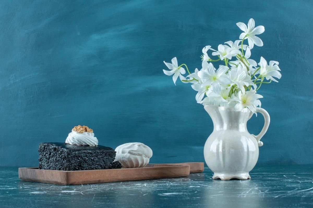 Cách cắm hoa ly trong bình sứ màu trắng bên cạnh là khay bánh ngọt trên nền tường xanh dương