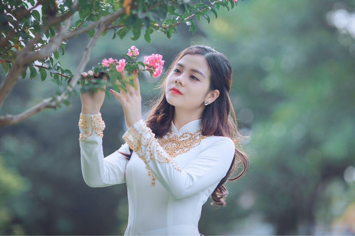 Mẫu áo dài cưới trắng mới và đẹp cô gái chạm tay vào bông hoa màu hồng