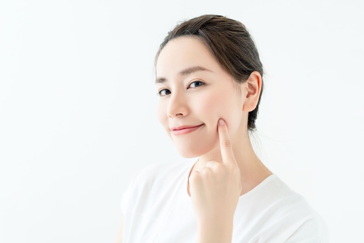 Cách trị mụn tự nhiên tại nhà cô gái chấm ngón tay lên má và mặc áo thun màu trắng phía sau là phông nền trắng