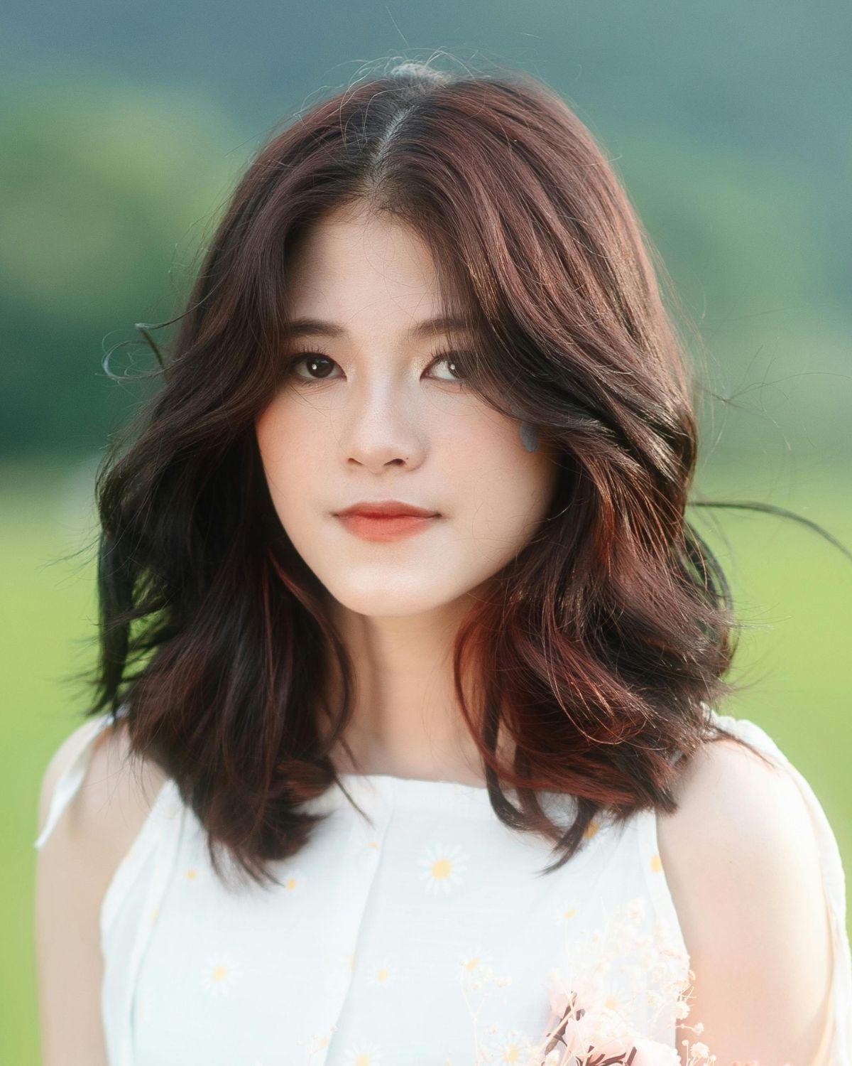 Tóc lỡ tóc lỡ uốn nhẹ rẽ ngôi giữa cô gái mặc váy màu trắng chụp ngoài trời phía sau bị làm mờ