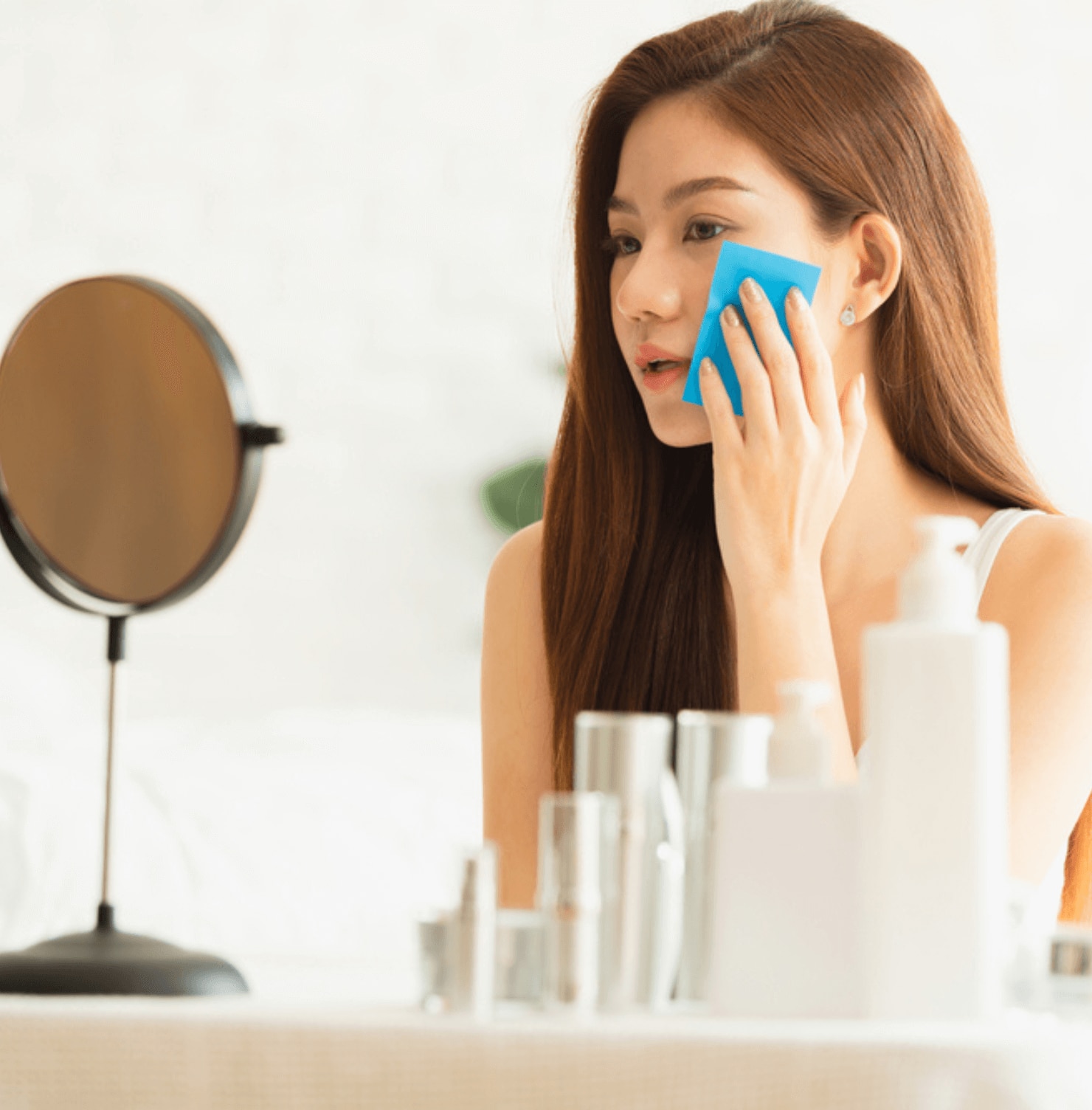 da dầu nguyên nhân gây da dầu cô gái soi gương tay cầm miếng giấy thấm dầu đặt lên lên má