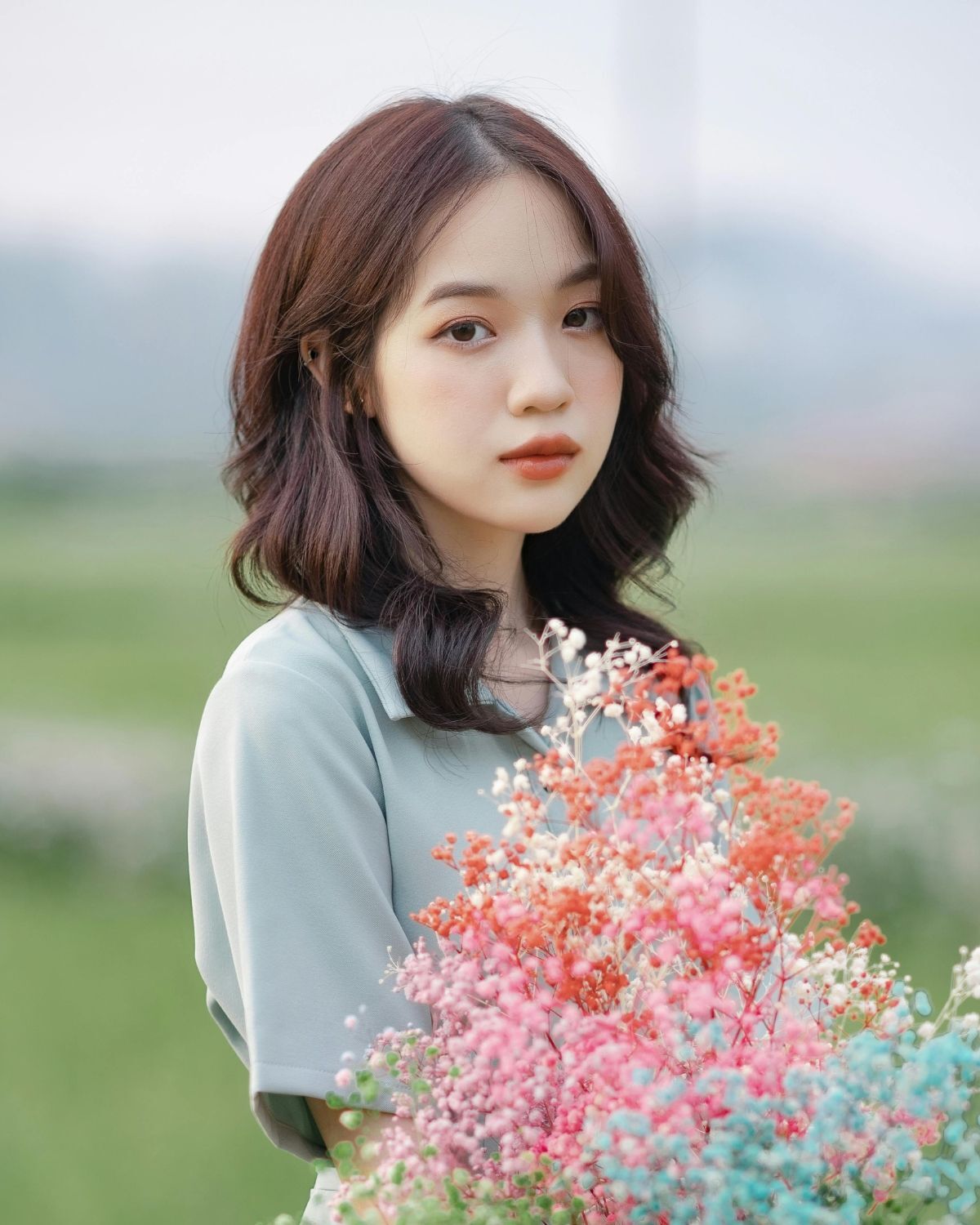 Tóc lỡ tóc lỡ uốn nhẹ rẽ ngôi giữa cô gái mặc váy màu xanh lá tay ôm bó hoa 