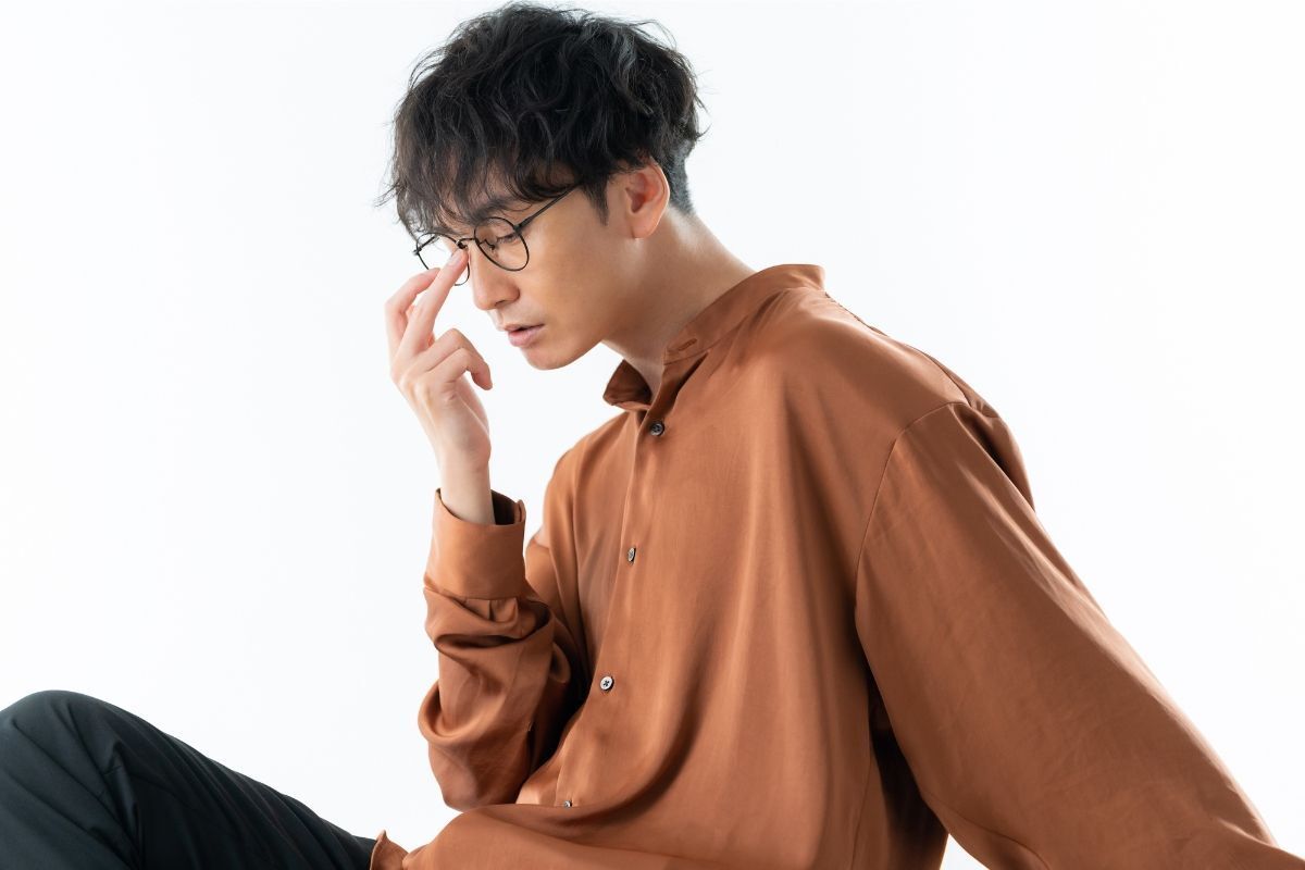 tóc layer nam uốn chàng trai tóc uốn đeo mắt kính mặc áo sơ mi màu cam đất ngồi tay để lên gọng kính