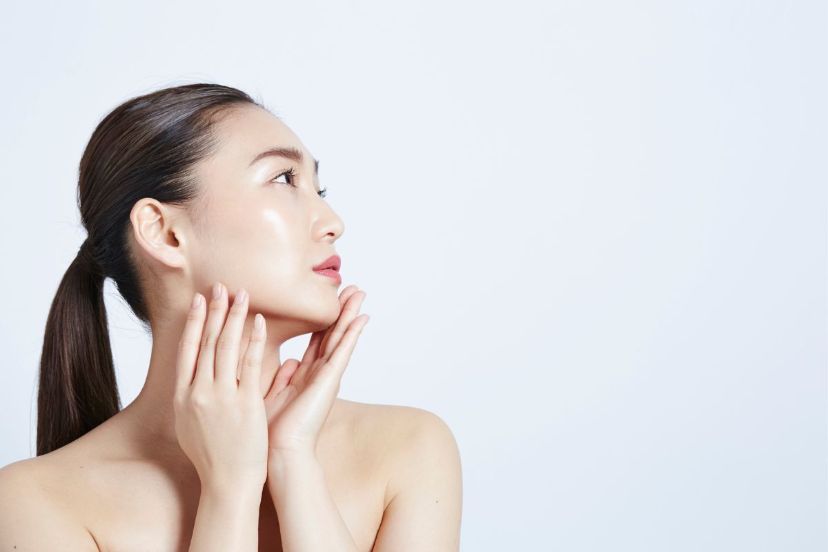 tác dụng phụ của retinol cô gái cột tóc đuôi gà da mặt căng bóng nhìn nghiêng hướng lên trên hai tay chạm nhẹ vào cằm