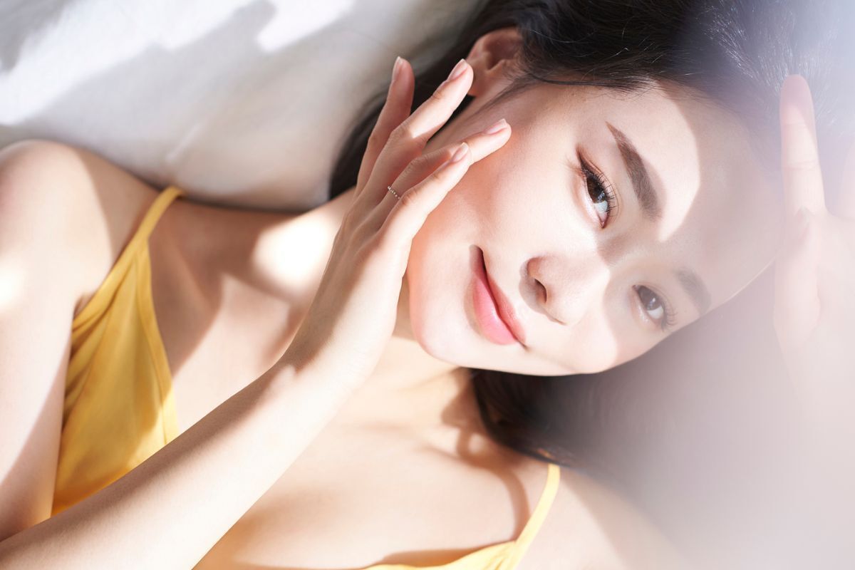 tác dụng phụ của retinol cô gái nằm nhìn thẳng cười mỉm, ngón tay chạm nhẹ vào má