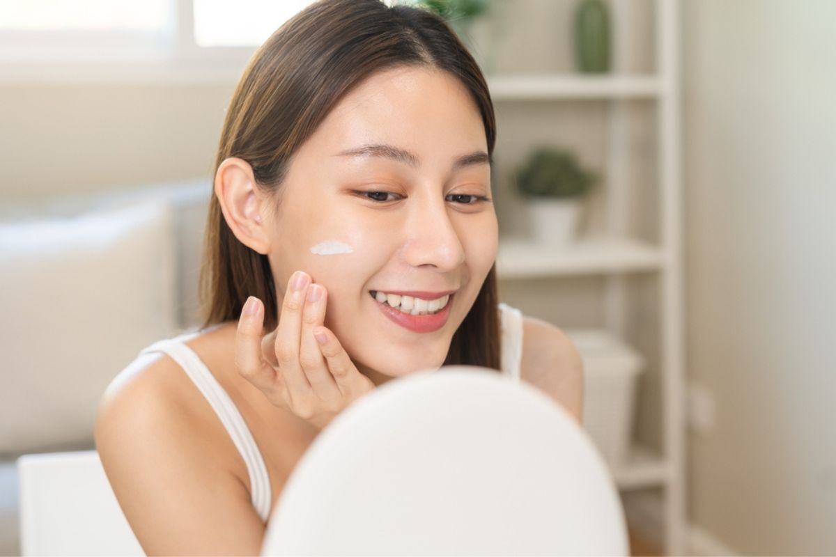 thải độc da mặt các cách thải độc da tăng cường và củng cố hàng rào bảo vệ da cô gái nhìn vào gương tròn tay thoa vệt kem màu trắng lên má bên phải