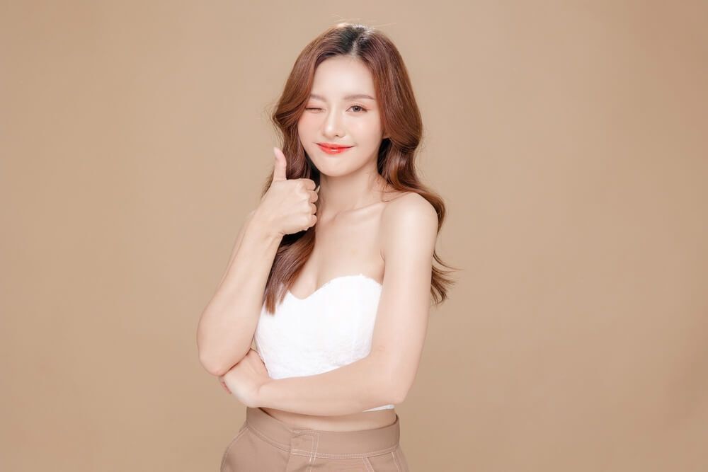 cách sấy tóc phồng mẹo sấy tóc giữ nếp dài lâu cô gái có mái tóc uốn xoăn sóng nước màu nâu đang giơ ngón tay cái