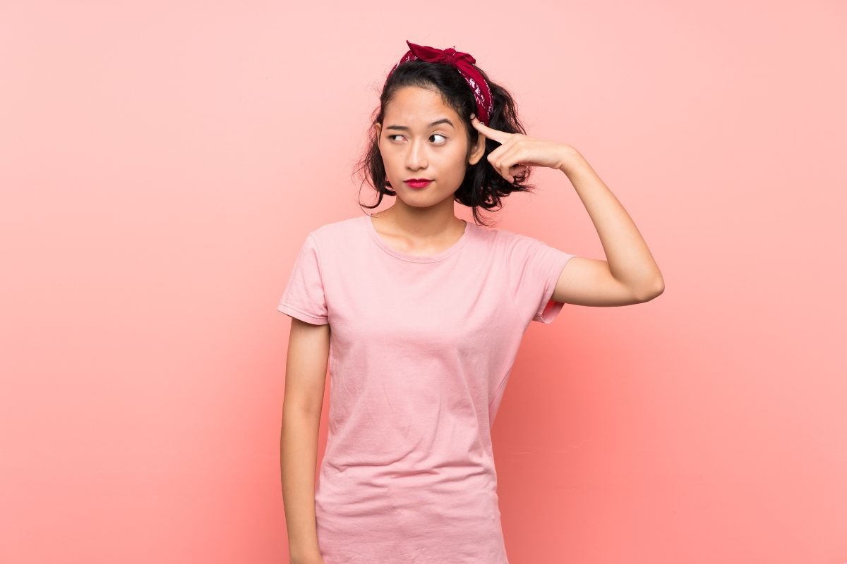 cà khịa là gì cô gái chỉ tay vào thái dương đang suy nghĩ một cách khó hiểu mặc áo hồng trên nền hồng