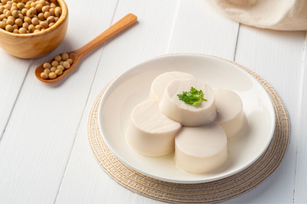 ăn gì để tóc mọc nhanh chất sắt đậu hũ dĩa đựng dậu hũ tròn kế bên hạt đậu nành đựng trong ly và muỗng trên nền gỗ trắng